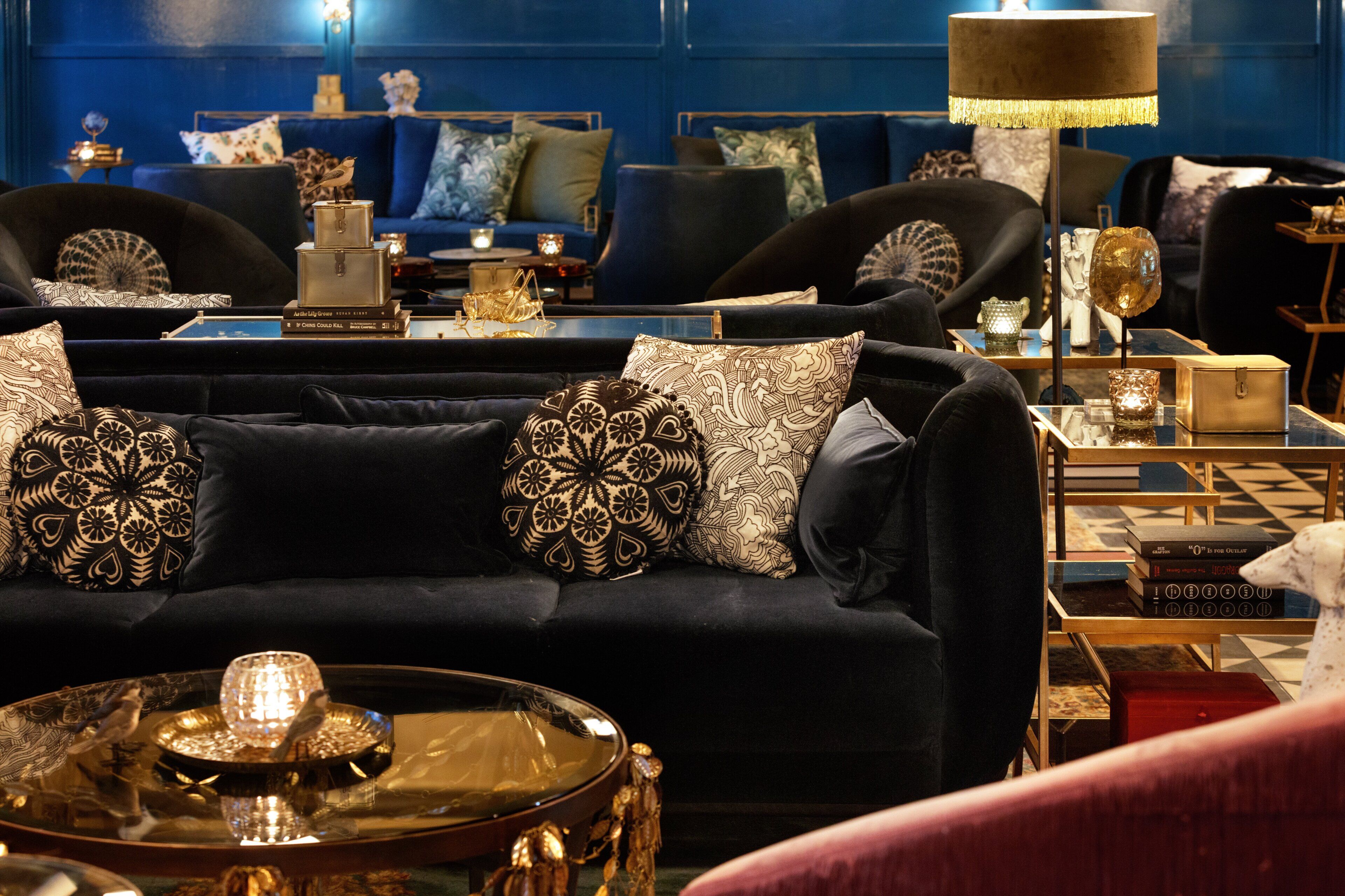 Een donkergrijze bank met gekleurde kussens, een rond glazen tafeltje met een decoratief object, en een lamp met een bies.