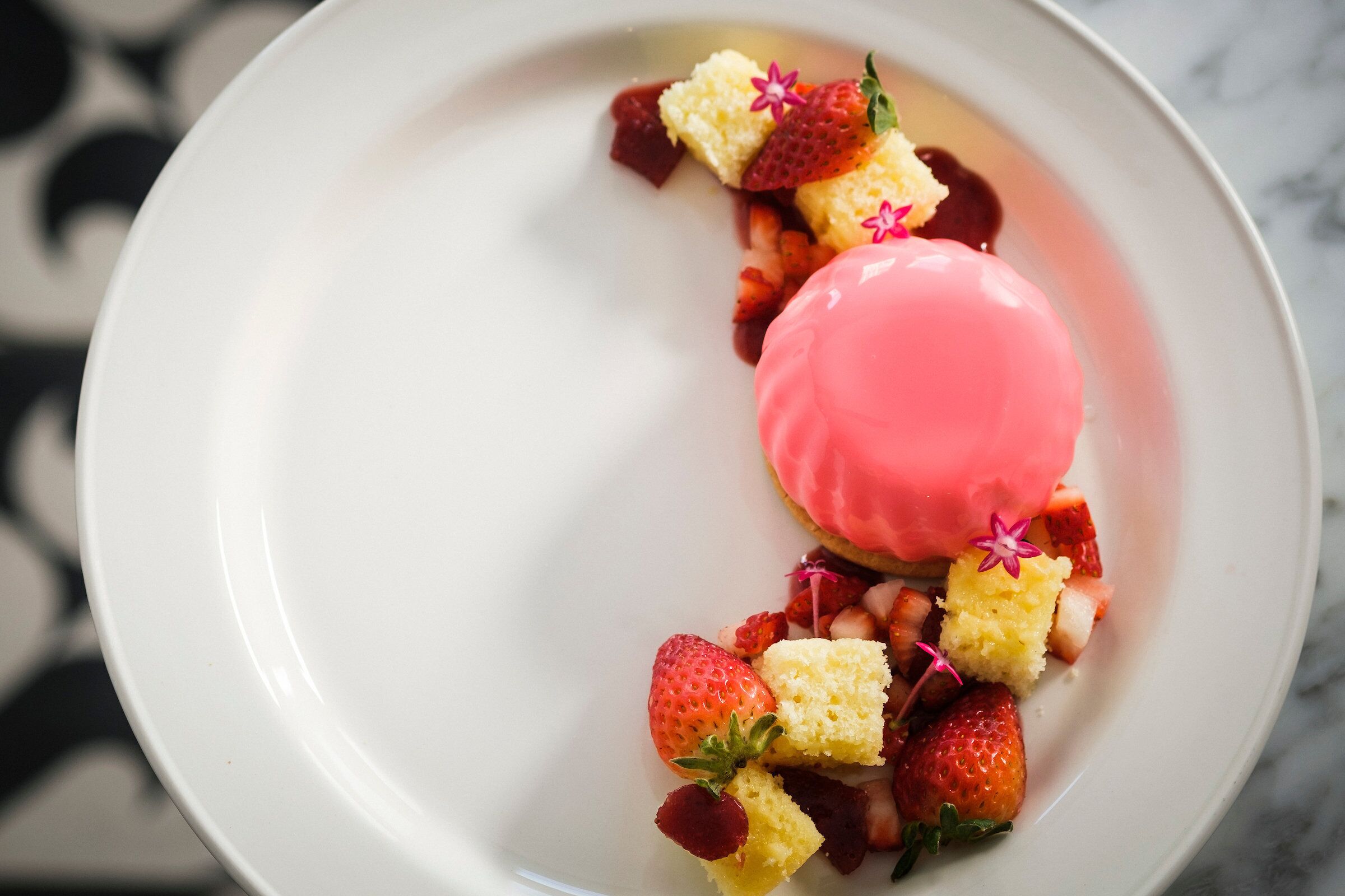 A dessert plate with a pink dome, strawberries, and small yellow cubes.