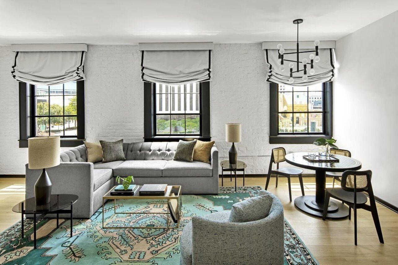 A modern living room with a grey sofa, a coffee table, a patterned rug, and a dining area with a table and chairs.