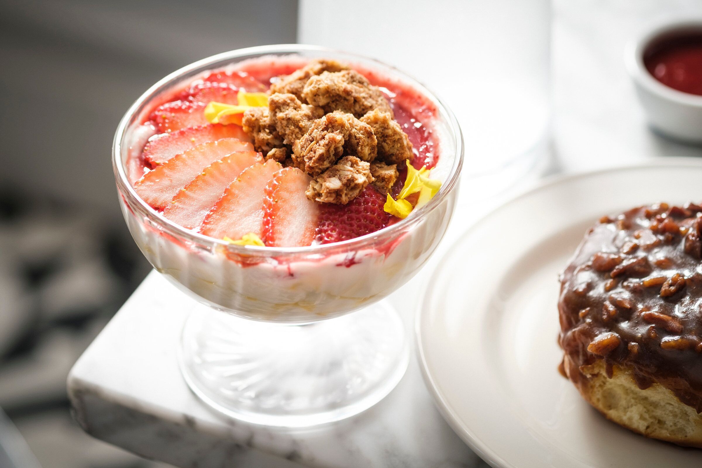Dessert in een glazen schaal met aardbeien en een koekje op een marmeren oppervlak.
