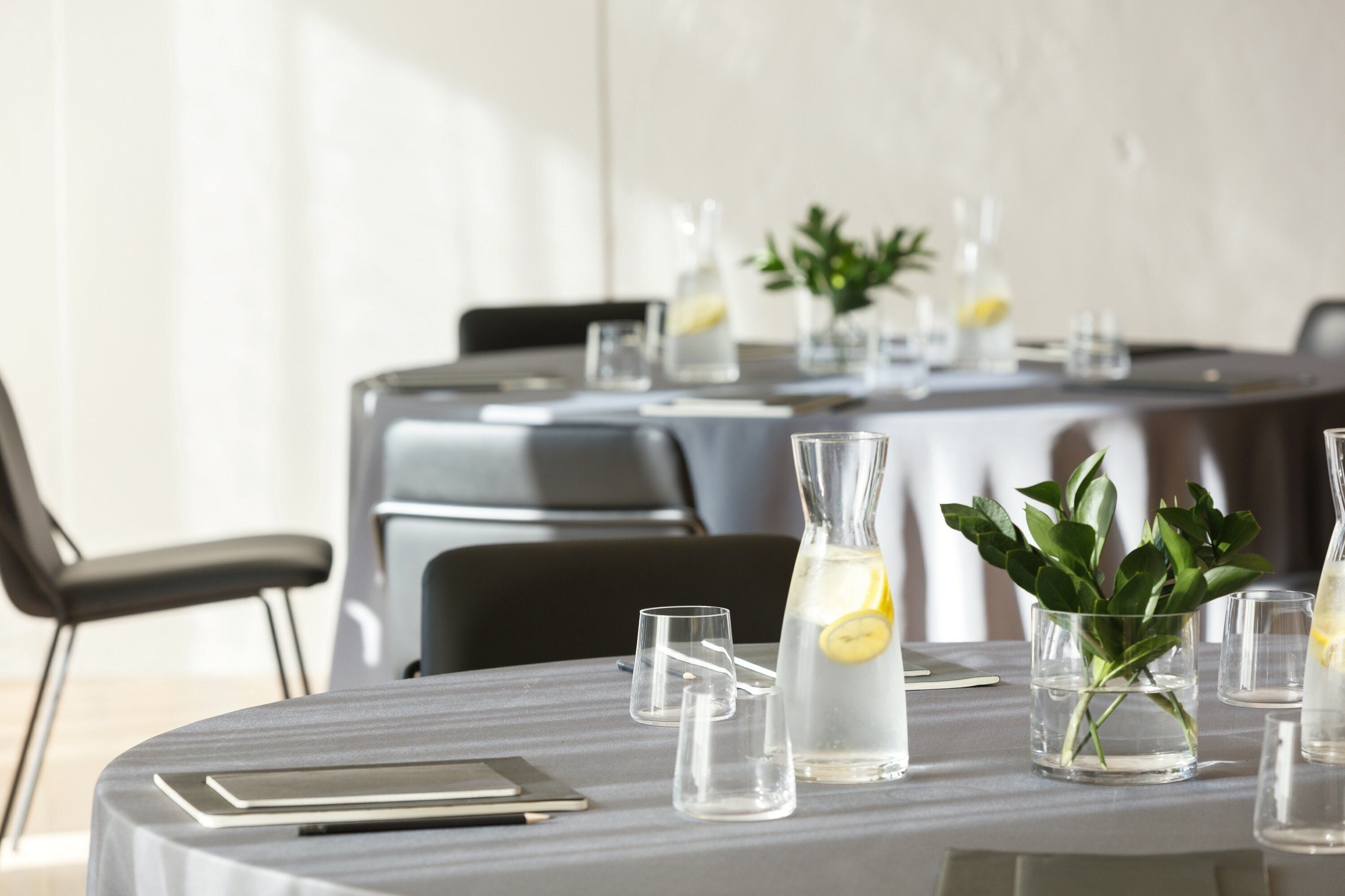 A table set for a meeting with clear glasses, a notebook, and a water bottle with a lemon slice.
