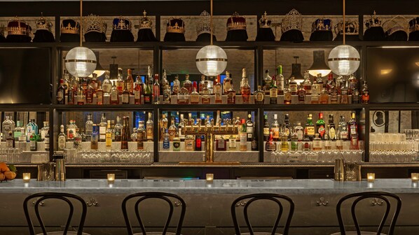 A bar area with multiple shelves of liquor bottles, a bar counter, and three chairs. - Kimpton Hotel Fontenot by IHG (New Orleans)