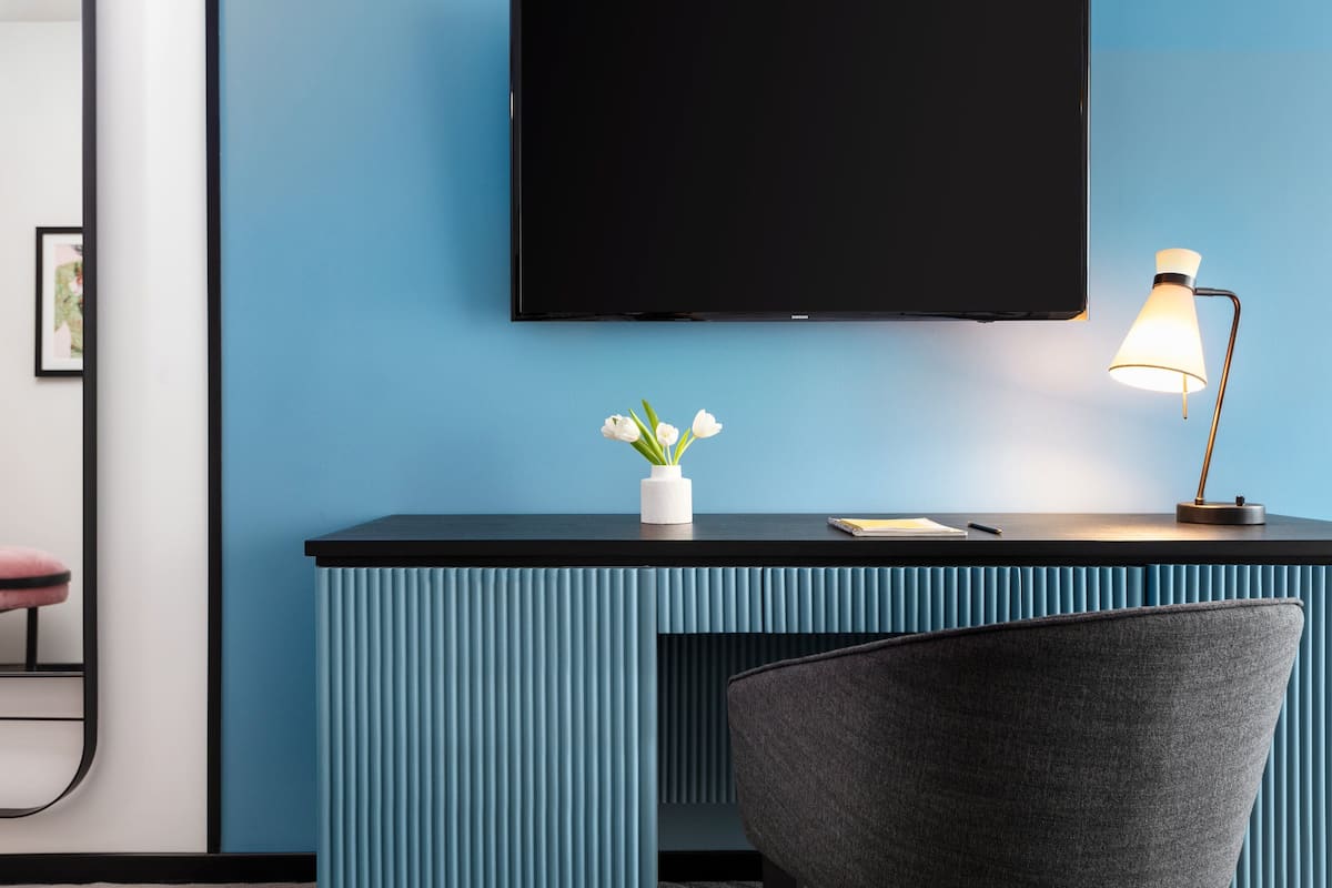 Ein modernes Zimmer mit blauer Wand, schwarzem Schreibtisch, weißer Vase mit Blumen, Lampe und Stuhl.