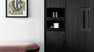 Una habitación con una obra de arte enmarcada en la pared, un armario negro con líneas verticales y un banco acolchado rosa.