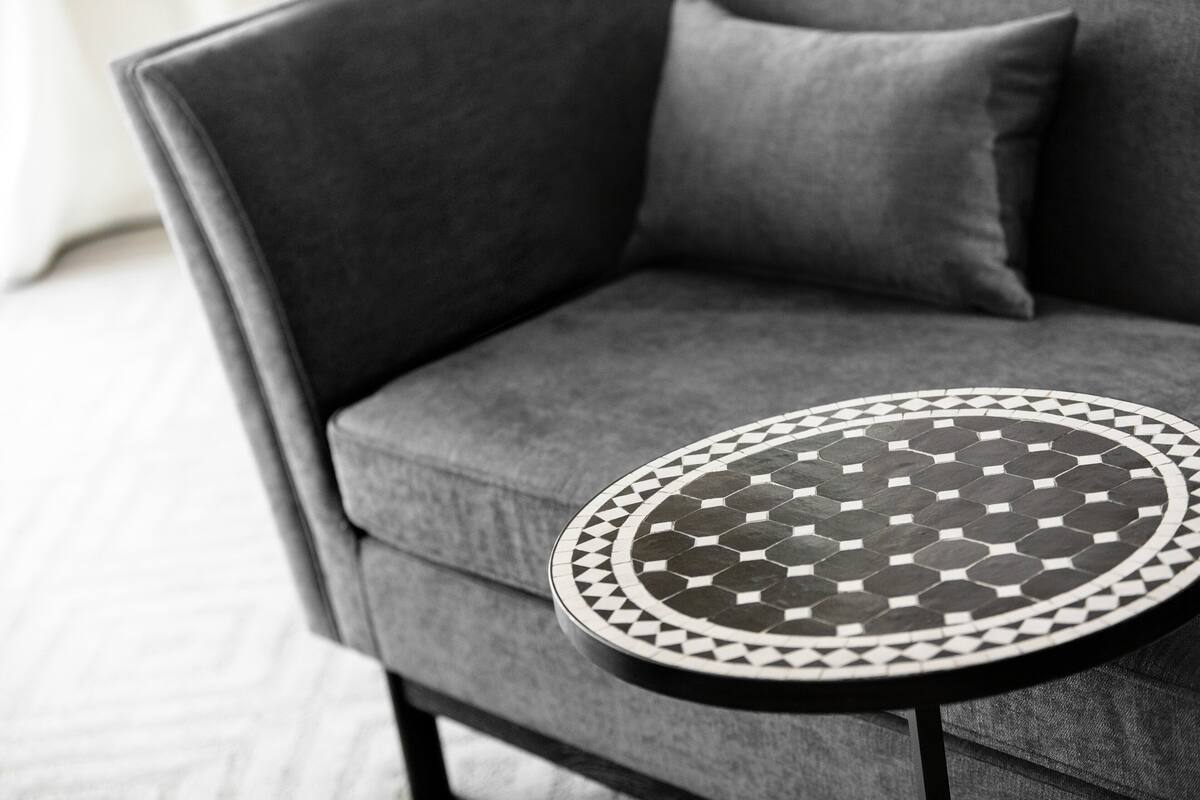 A grey sofa with a round black and white patterned table in front of it.