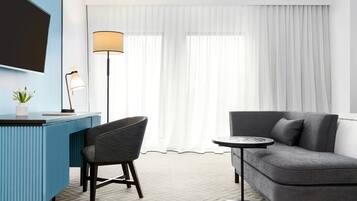 Una habitación de hotel moderna con un escritorio azul, un sofá gris, una pequeña mesa redonda y una lámpara de pie.
