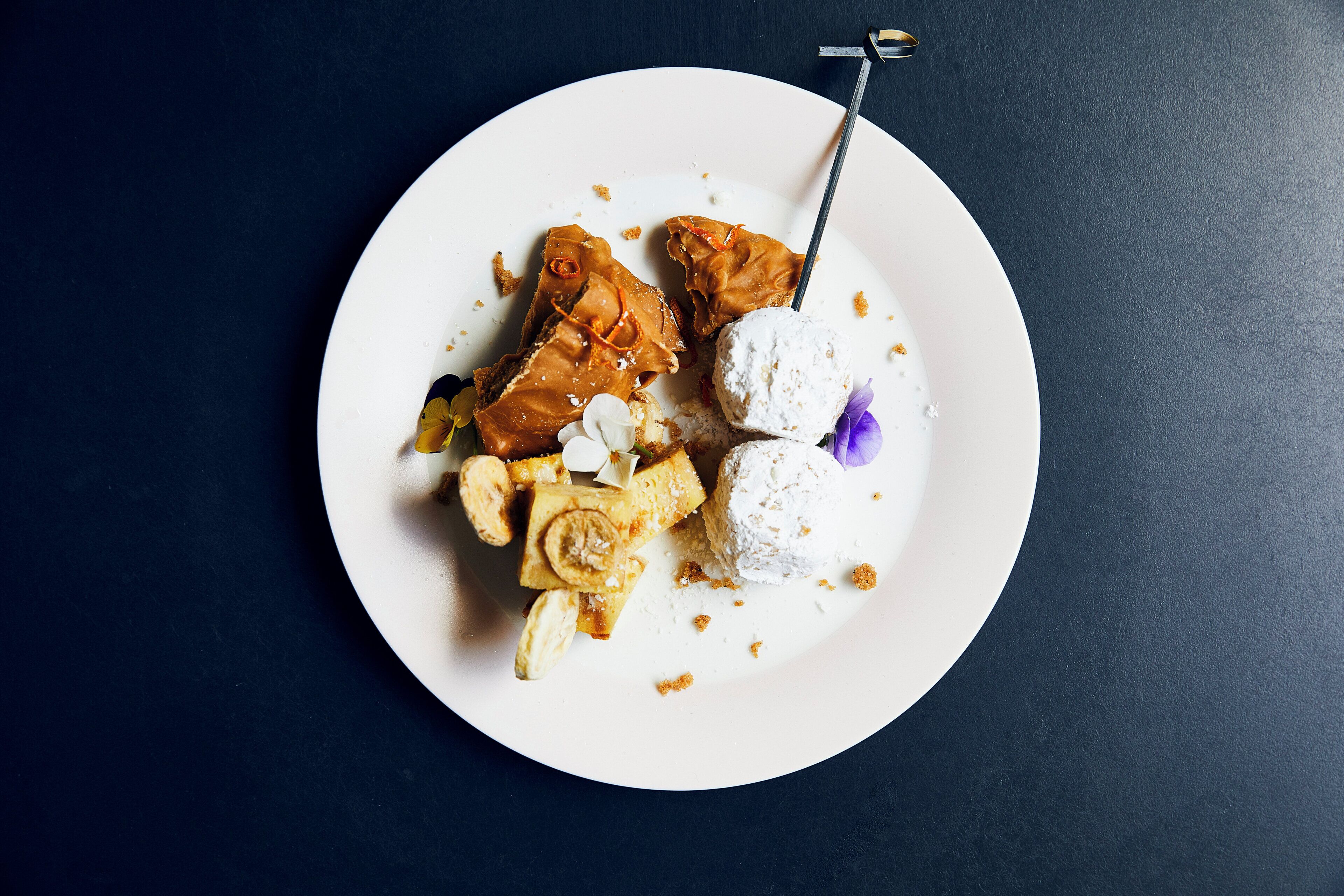 Une assiette blanche sur laquelle sont disposés différents desserts, le tout posé sur une surface sombre.