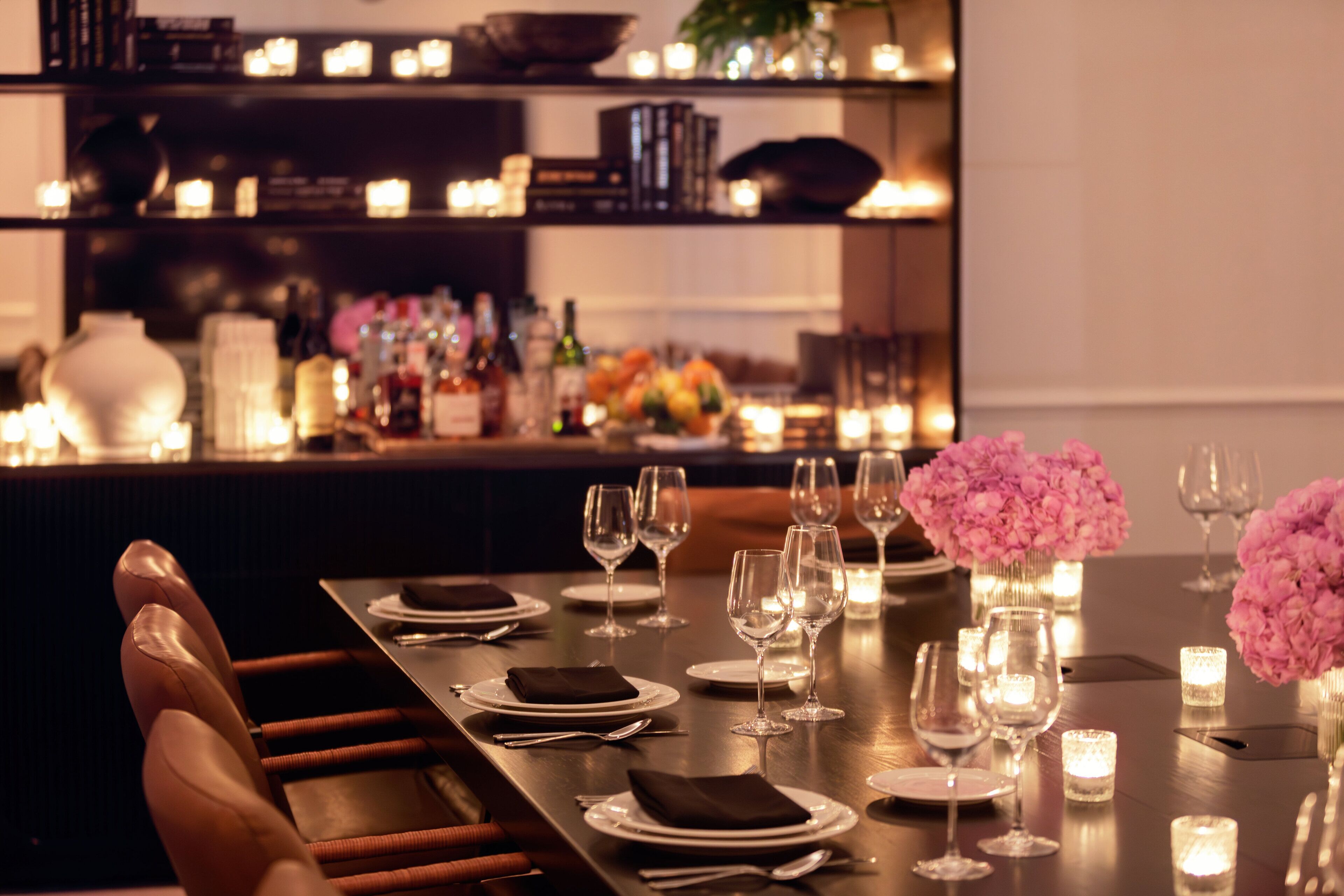 Una mesa de comedor bien dispuesta con velas, copas y un jarrón de flores.