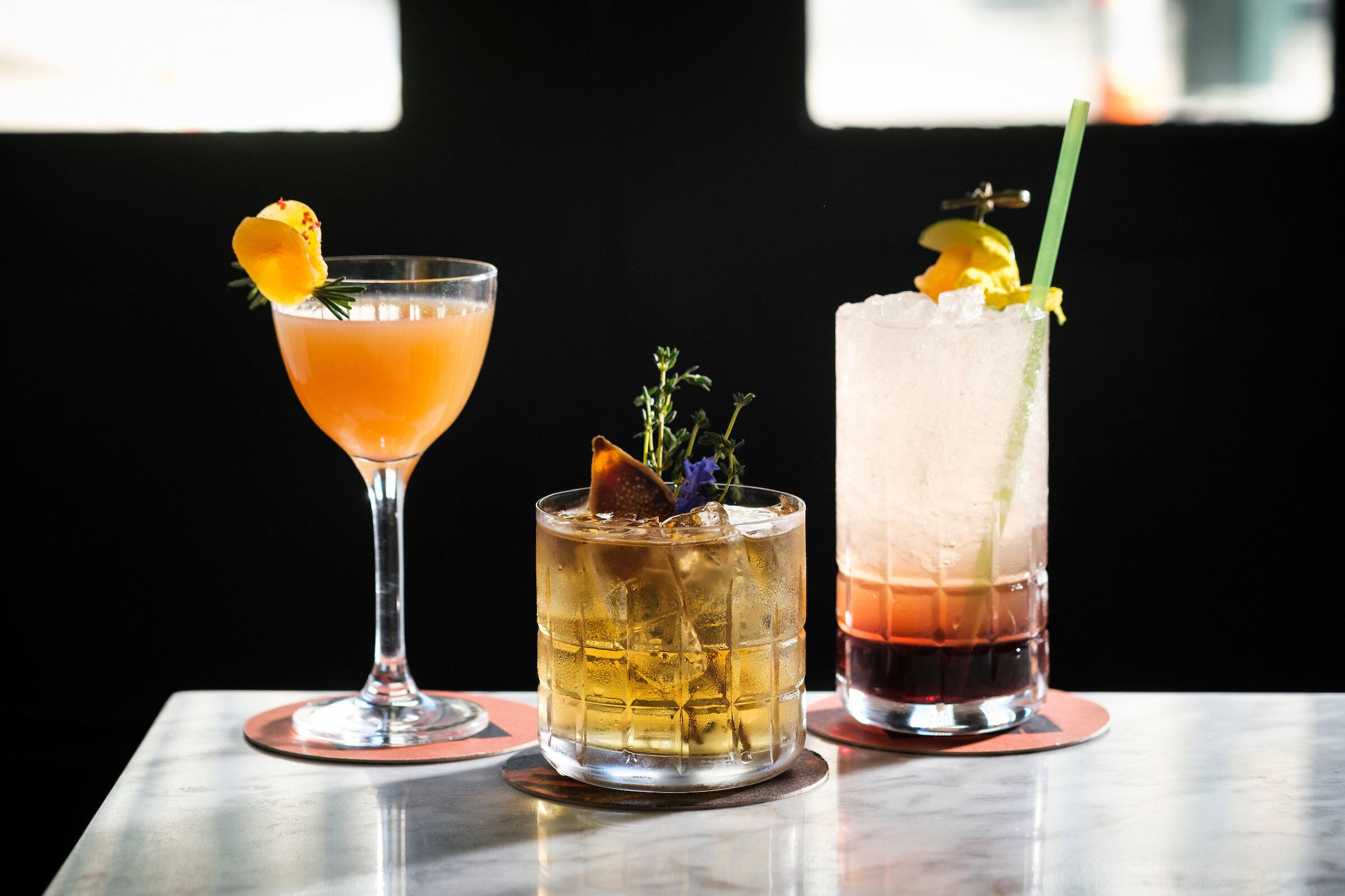 Three cocktails on a table with a dark background.