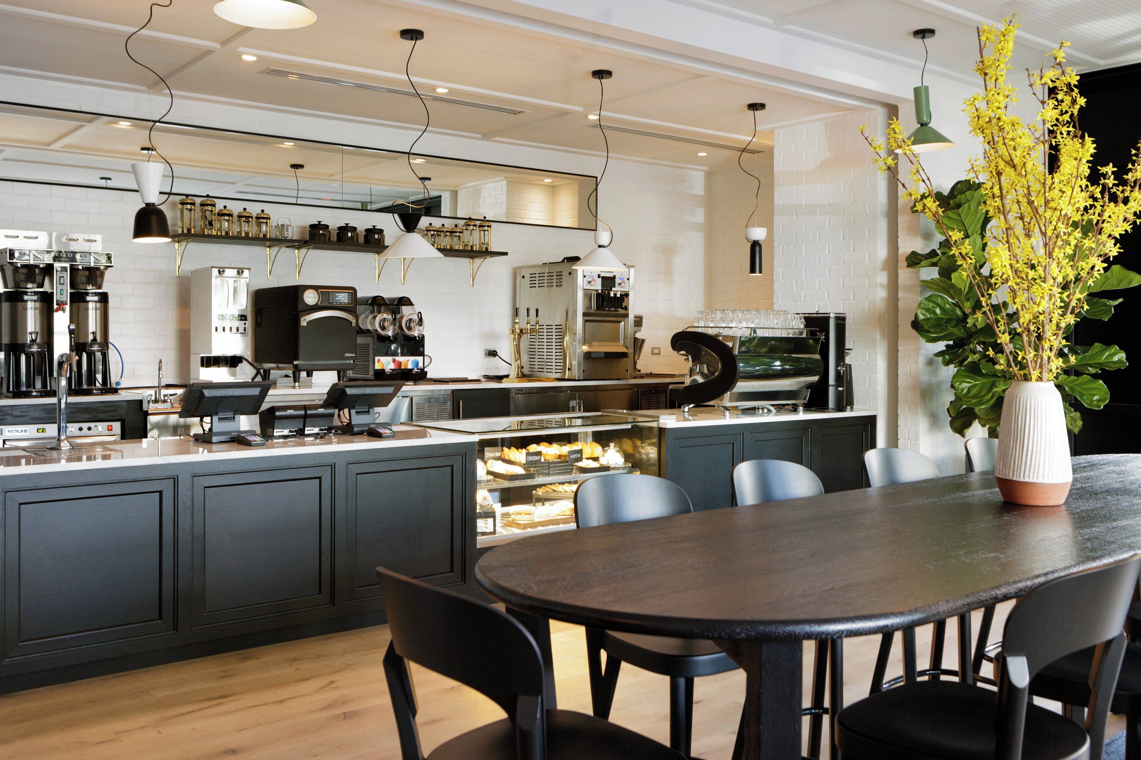En modern caféinredning med en central ö, sittområde och kaffemaskiner.