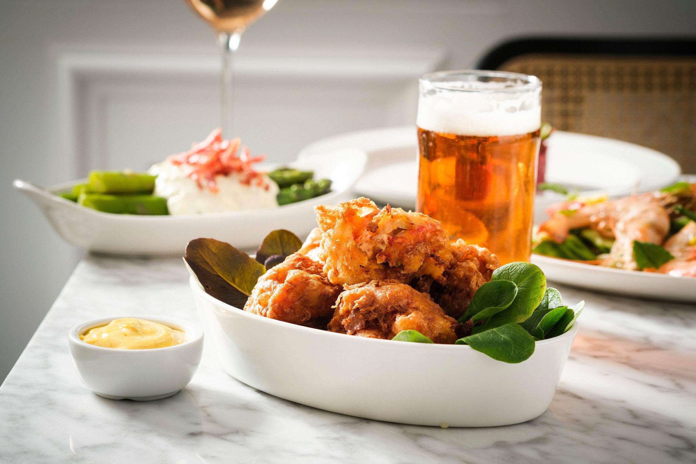 Una mesa de comedor con un plato de pollo frito, una jarra de cerveza y un recipiente pequeño con salsa.