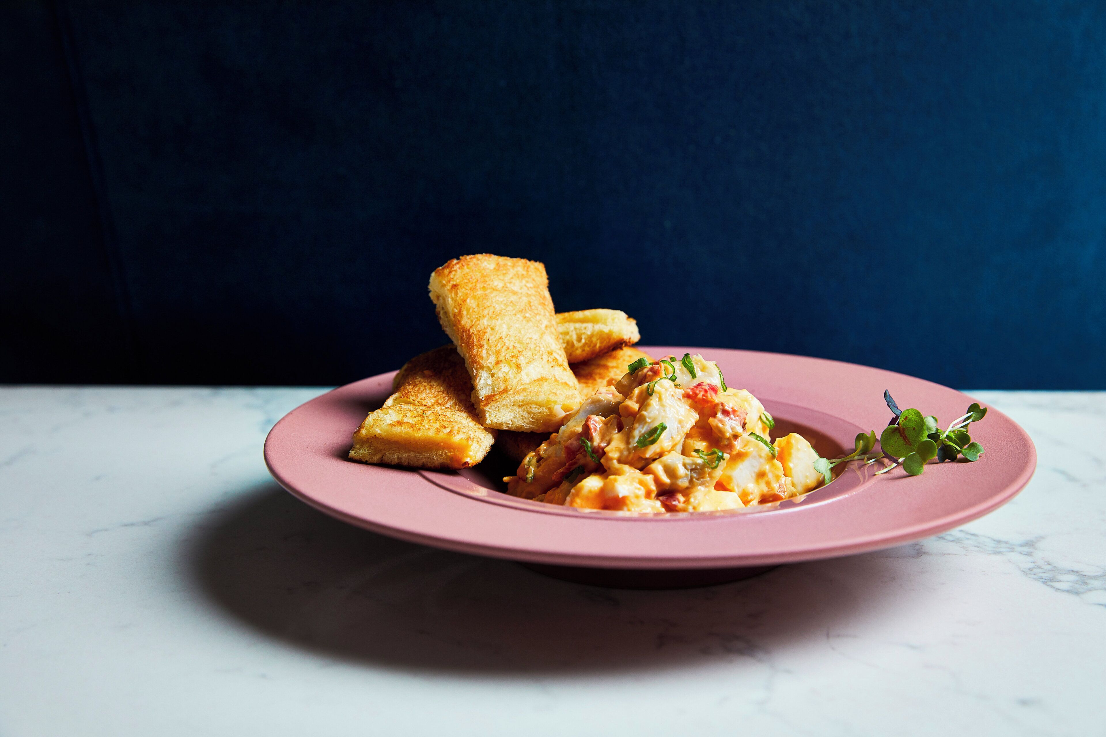 A plate with grilled cheese sandwiches and a side of scrambled eggs on a pink plate.