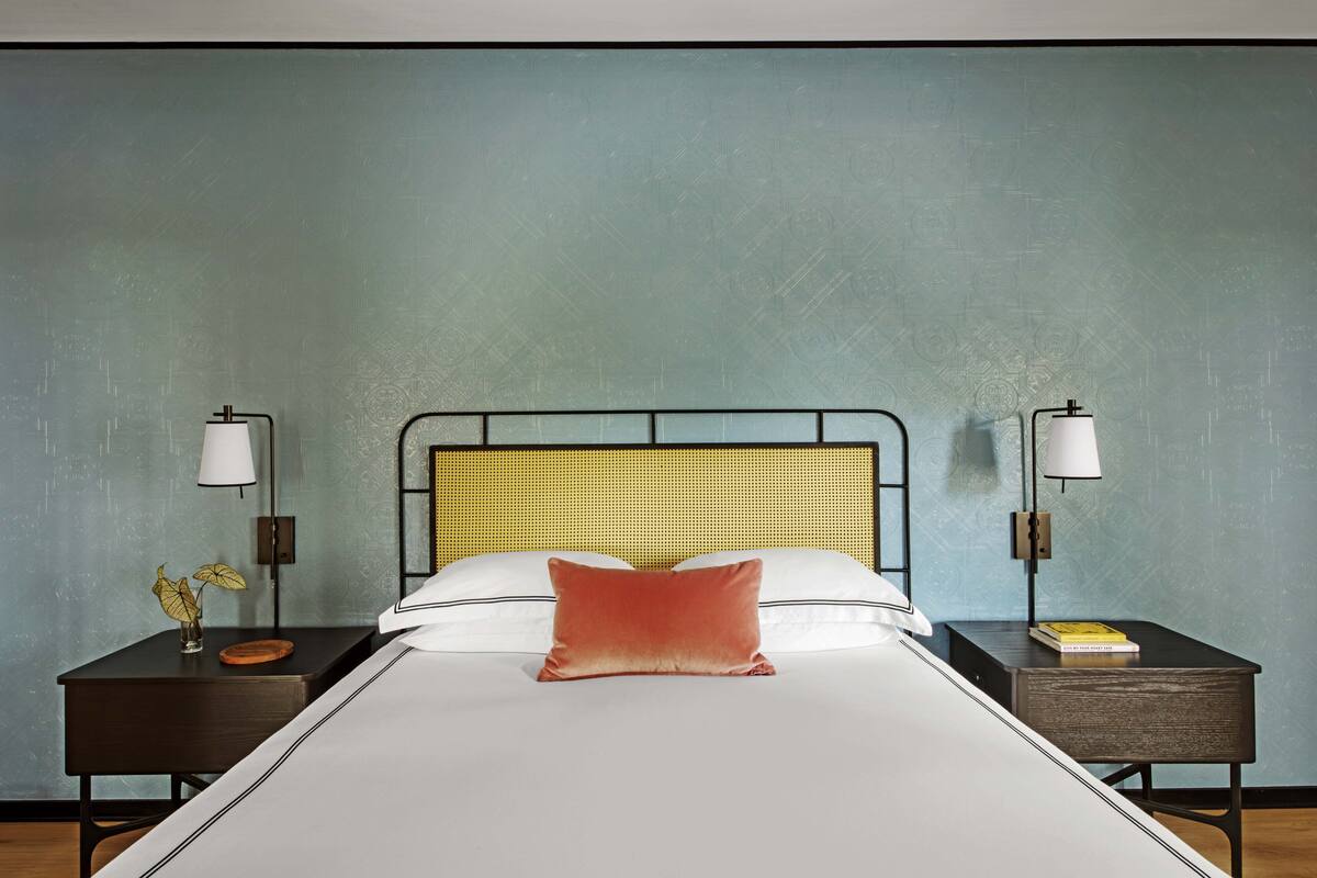 Ein Hotelzimmer mit einem Bett, zwei Nachttischen, einer Lampe und einer Wand mit strukturierter Oberfläche.