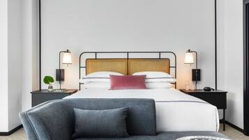 A modern hotel room with a bed, two bedside tables, a sofa, and a round coffee table.