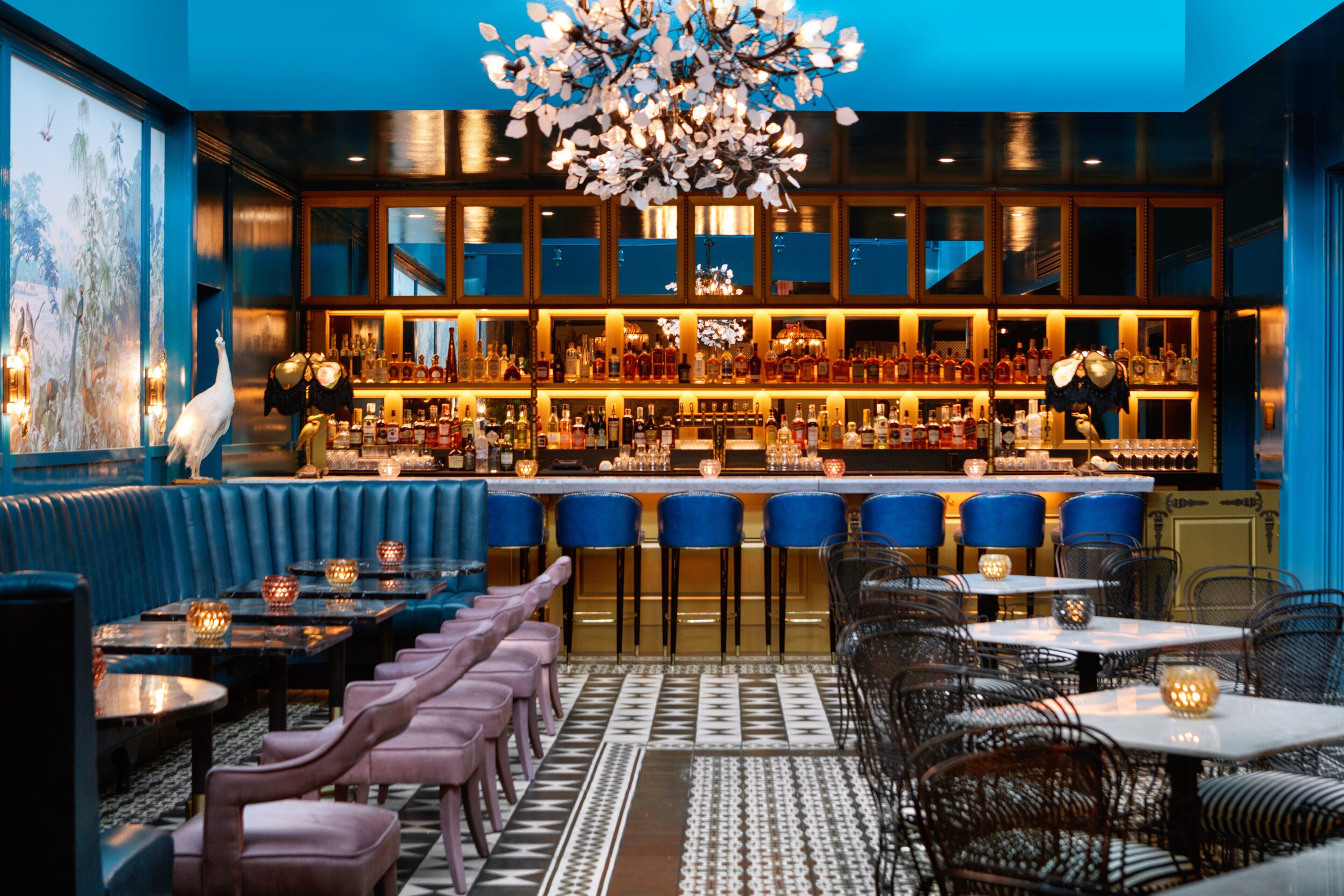 Un espace bar doté d’un plafond haut, de murs bleus et de différents types de sièges, notamment des tabourets de bar et des tables.
