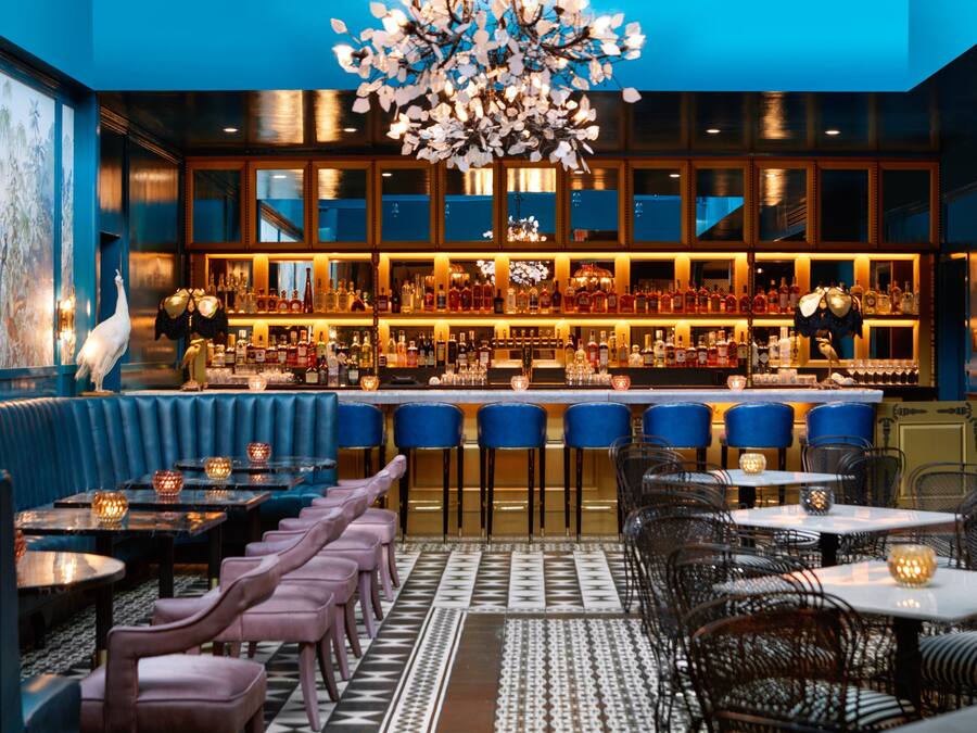 A bar area with a high ceiling, blue walls, and a variety of seating options including bar stools and tables.