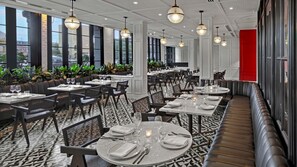 A restaurant with a modern interior, featuring black and white patterned flooring, round tables with white tablecloths, and black chairs. - Kimpton Hotel Fontenot by IHG (New Orleans)