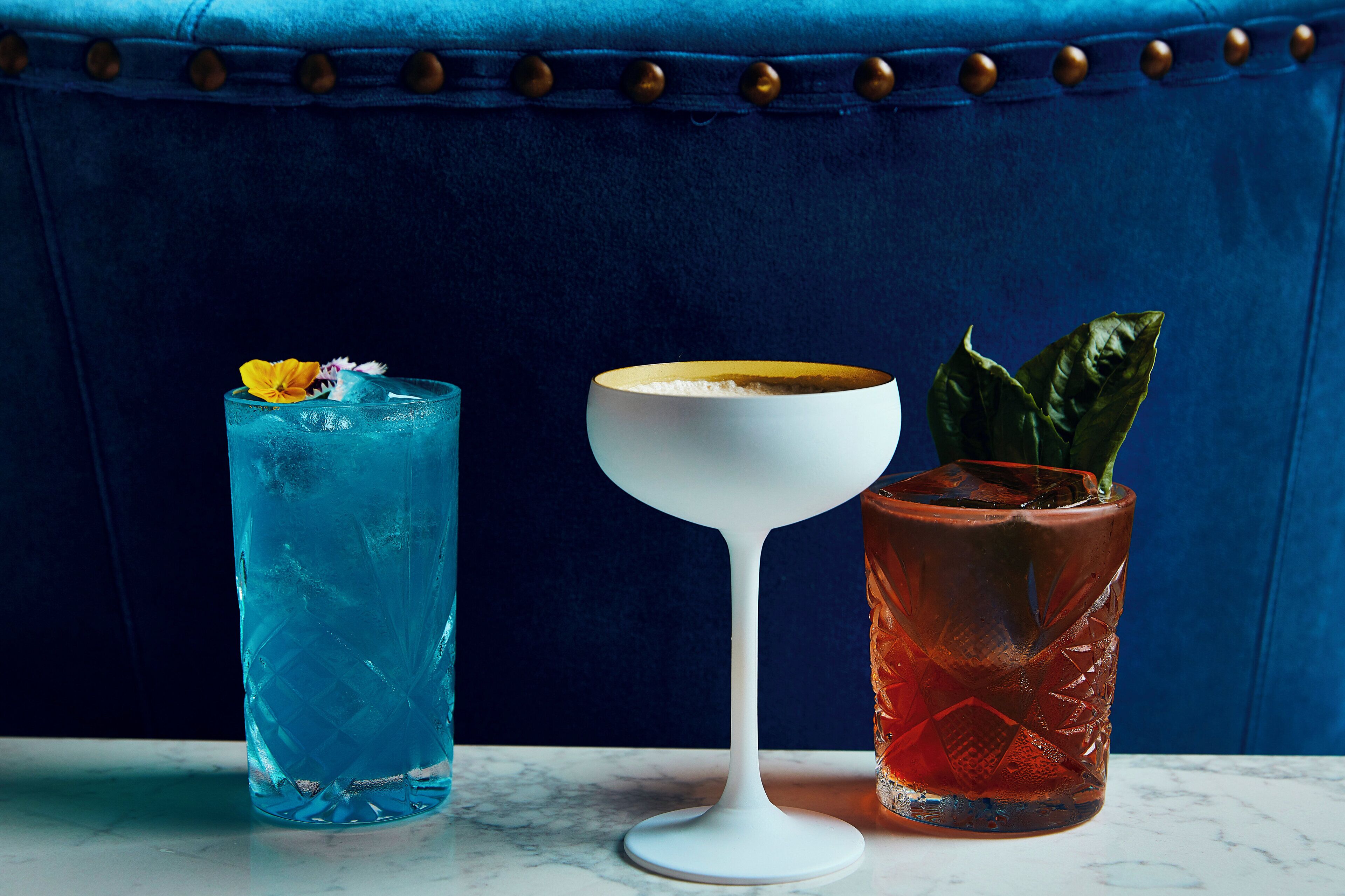 Tres bebidas sobre una superficie de mármol con un fondo tapizado en azul.