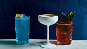 Tres bebidas sobre una superficie de mármol con un fondo tapizado en azul.