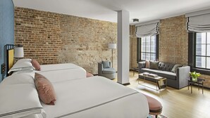 A modern hotel room with a brick wall, a sofa, a bed, and a window with curtains. - Kimpton Hotel Fontenot by IHG (New Orleans)