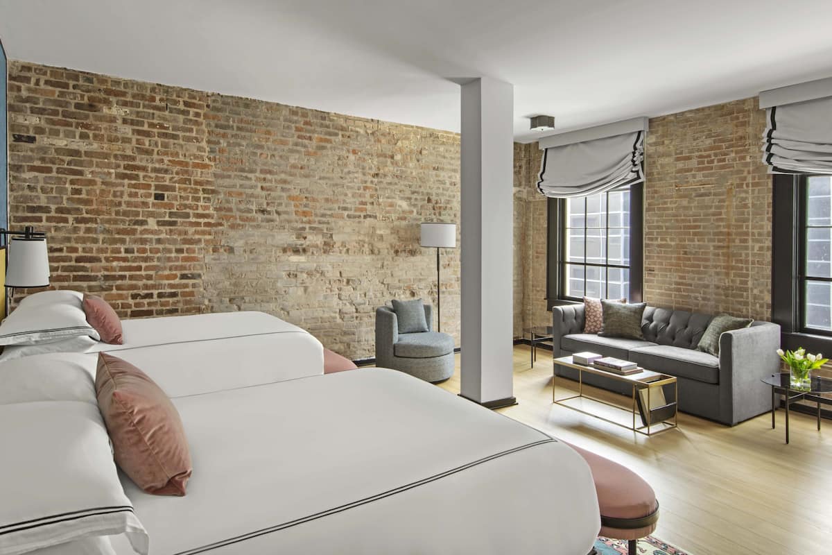 A modern hotel room with a brick wall, a large bed, a sofa, and a small table.