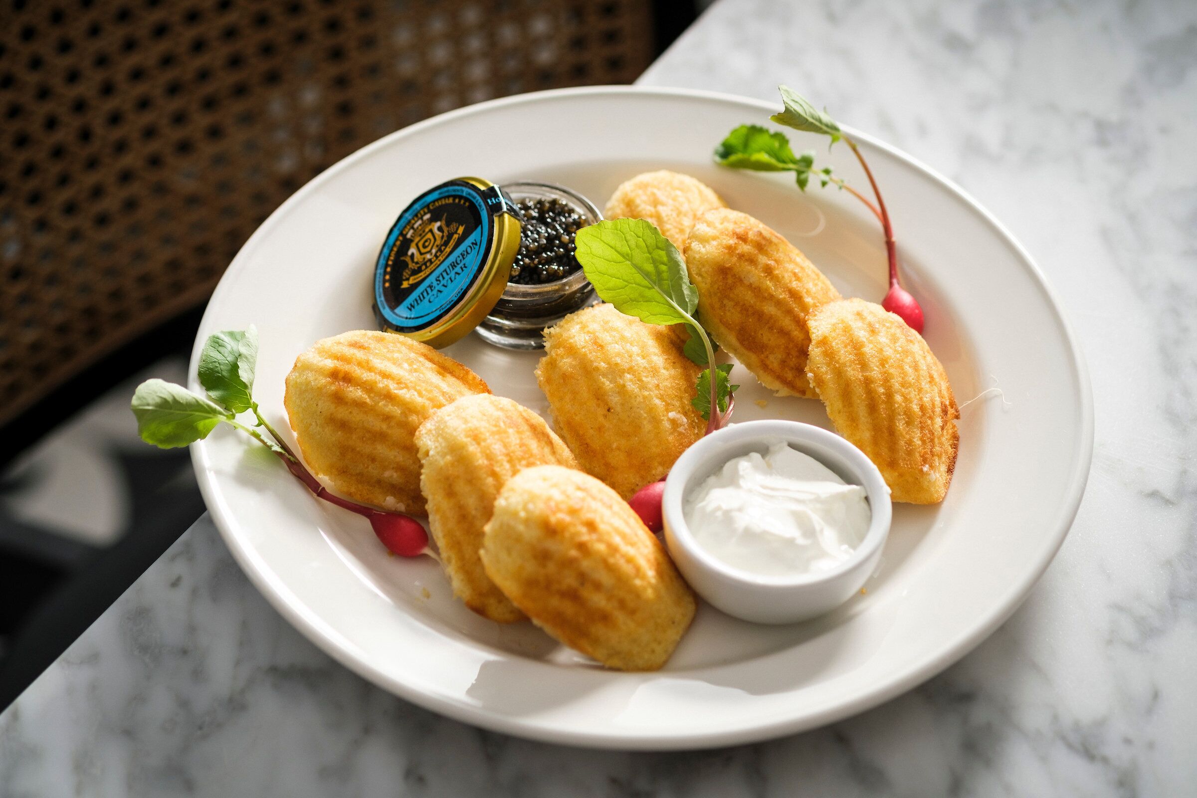 A plate of croquettes with a dipping sauce and a small container of black caviar.