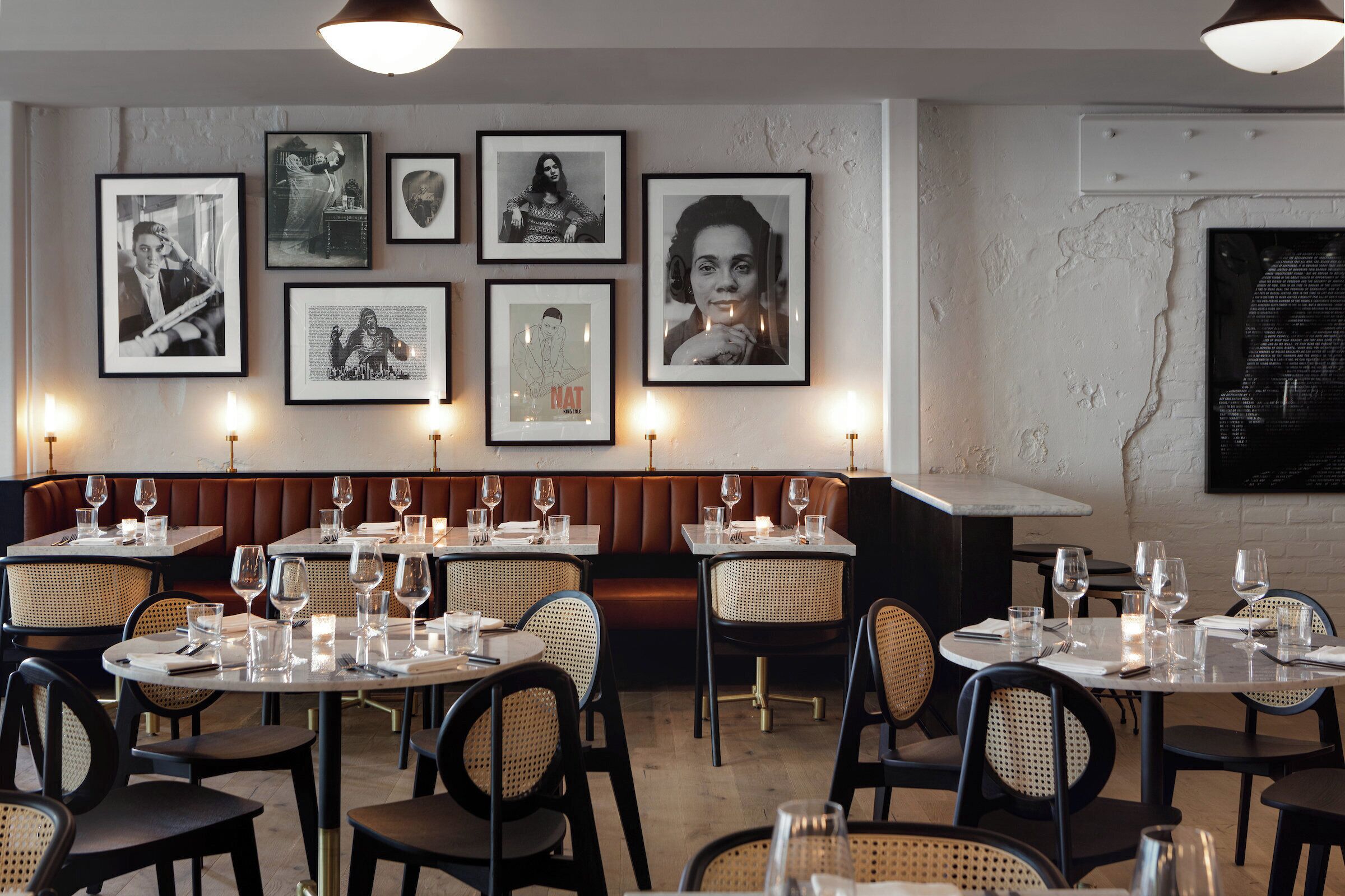Un restaurante con mesas redondas, sillas de mimbre y un banco con cojín marrón.