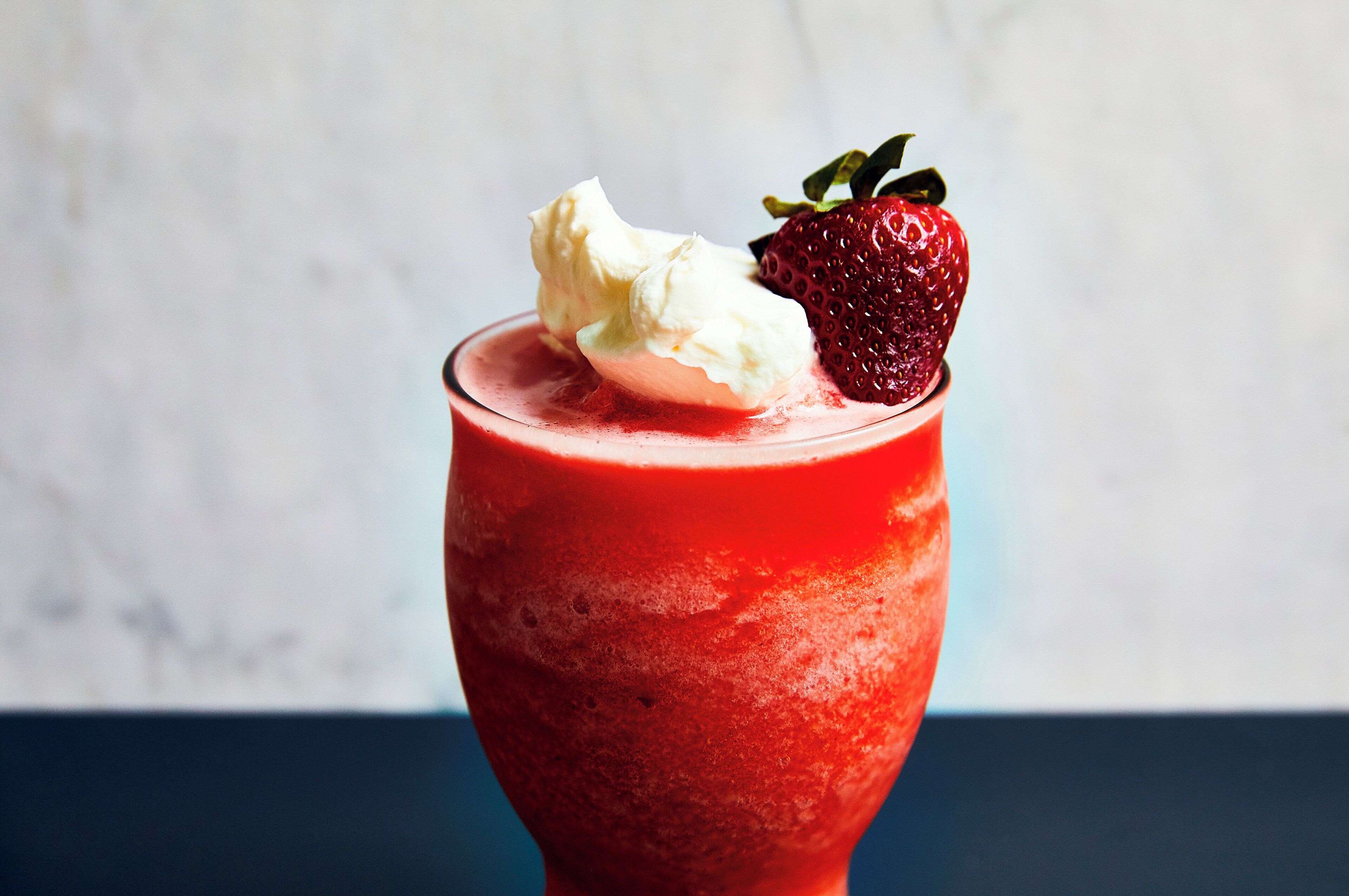 Un verre d’une boisson rouge, avec une fraise et une boule de glace sur le dessus.