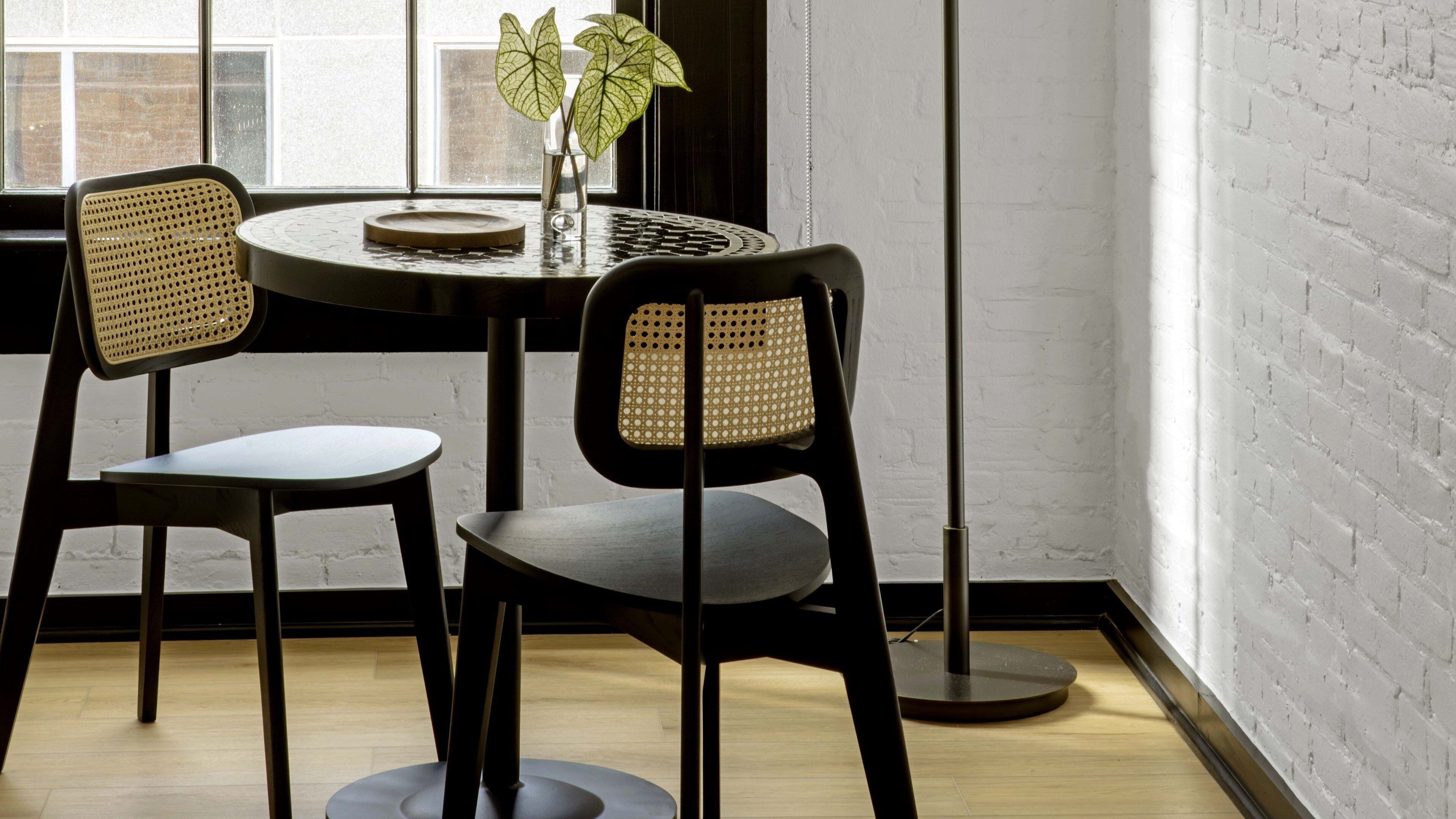 A dining area with two chairs and a table, a potted plant, and a window with a view of a brick building.