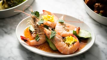 A plate of cooked shrimp garnished with mint leaves and a yellow flower, served on a white plate.