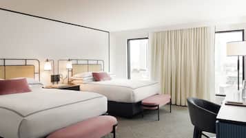 Une chambre d’hôtel avec deux lits, un bureau, une chaise et une grande fenêtre avec des rideaux.