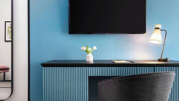 Una habitación moderna con pared azul, un escritorio negro, un jarrón blanco con flores, una lámpara y una silla.