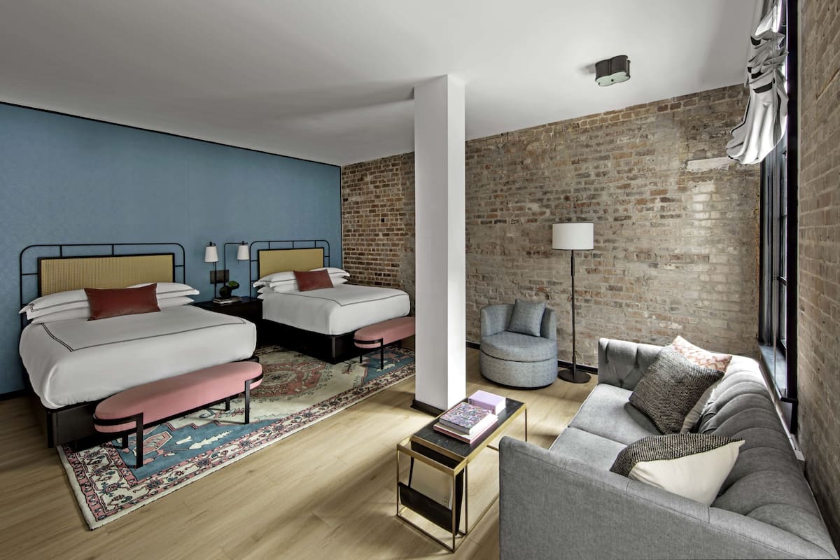 Ein modernes Hotelzimmer mit zwei Betten, einem Schlafsofa, einem kleinen Tisch und einer Ziegelwand.