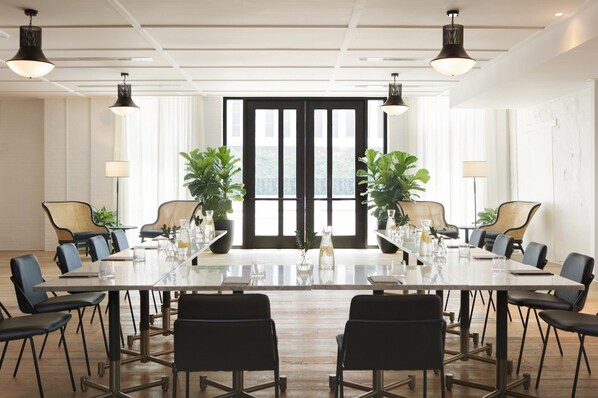 A conference room with a long table, black chairs, and potted plants.