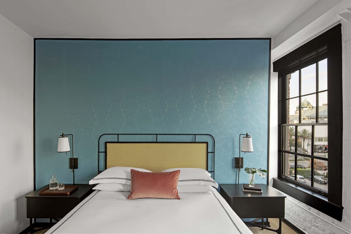 Ein modernes Hotelzimmer mit einem großen Bett, zwei Nachttischen und einem Fenster mit Blick auf die Stadt.