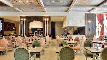 A grand dining area with ornate chandeliers, plush seating, and a bar area visible through an open doorway.