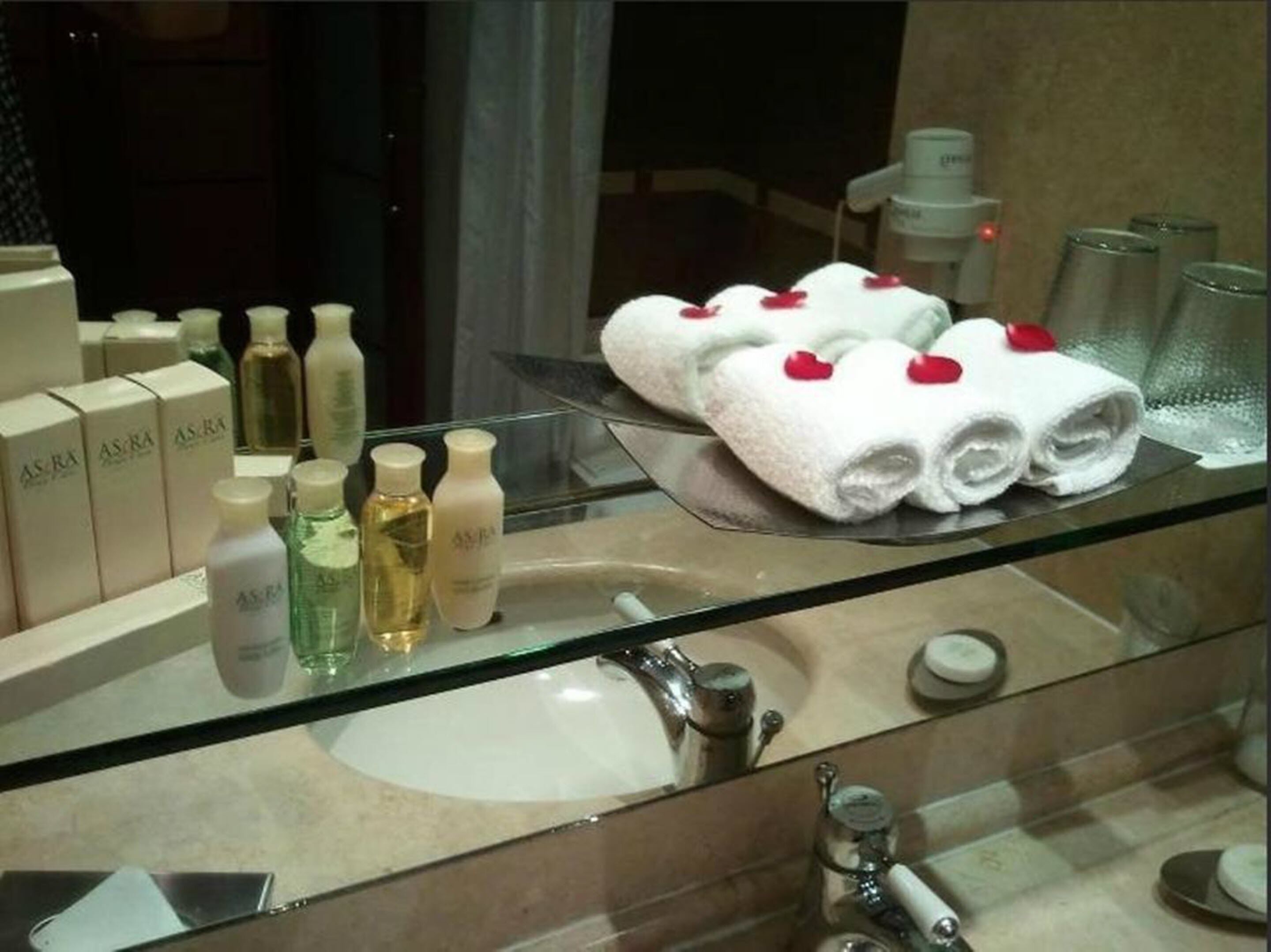 A bathroom with a glass sink, toiletries, and towels on a tray.