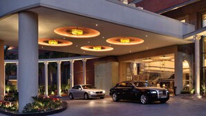 A hotel entrance with a covered area, columns, and two cars parked in front. - Radisson Blu Hotel Noida (Noida)