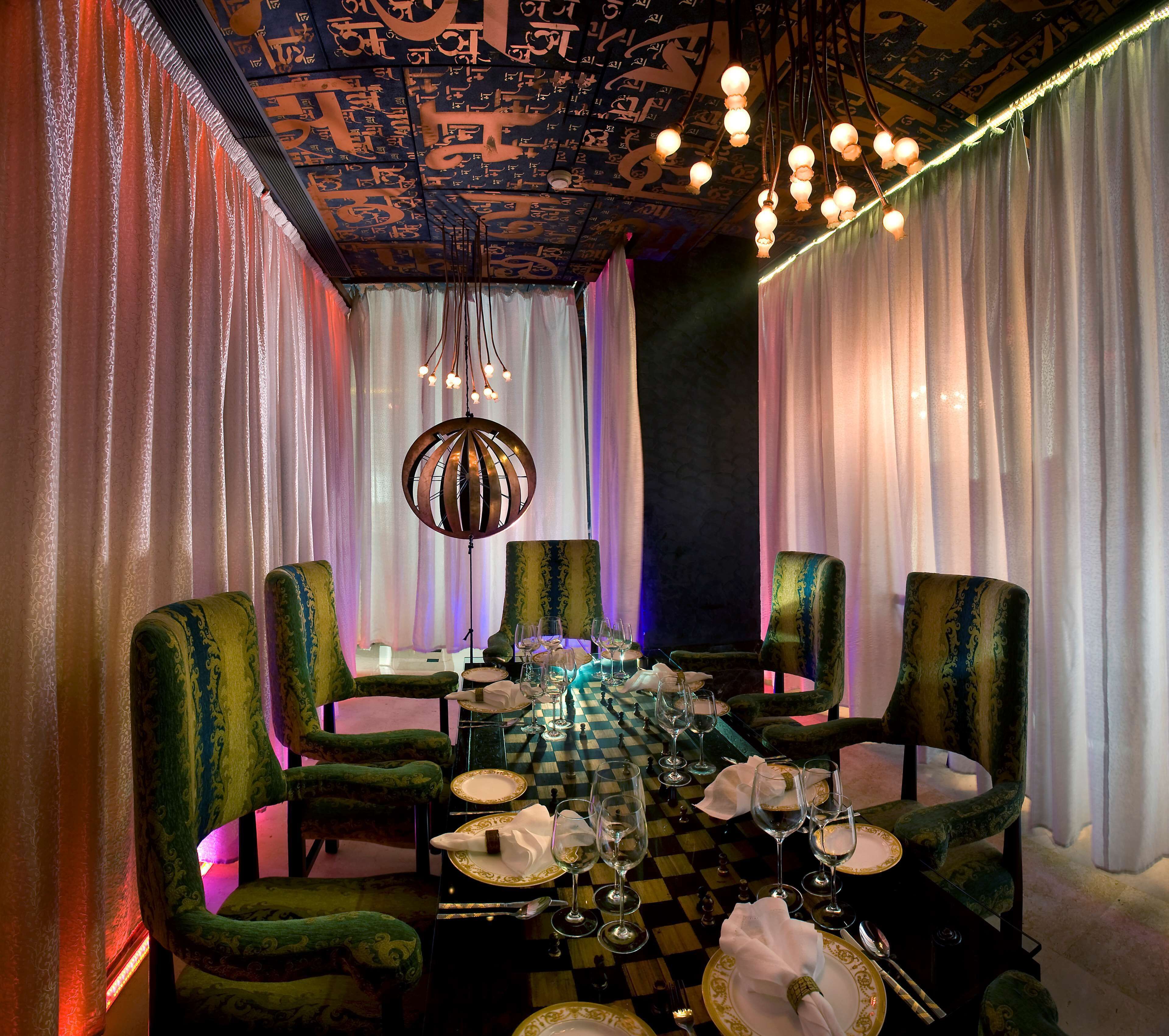 A dining area with a checkered tablecloth, green upholstered chairs, and a chandelier.