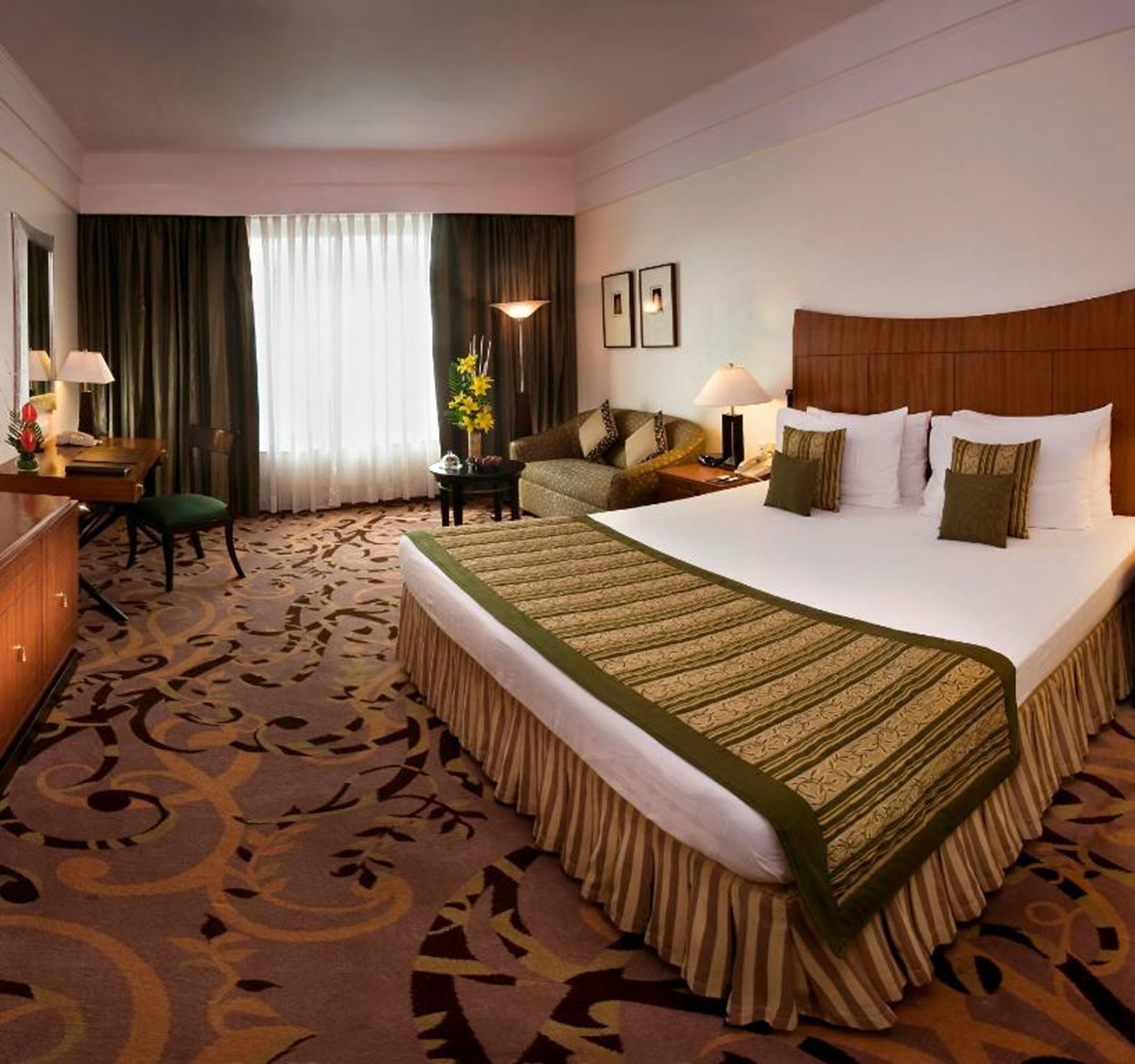 A hotel room with a large bed, a desk, a chair, a nightstand, and a lamp.
