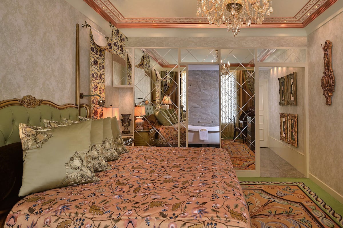 A luxurious bedroom with a large bed, ornate furniture, and a chandelier.