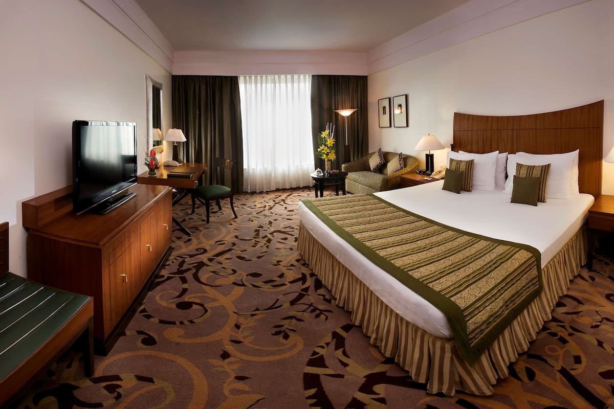A hotel room with a large bed, a television, a desk, and a chair.