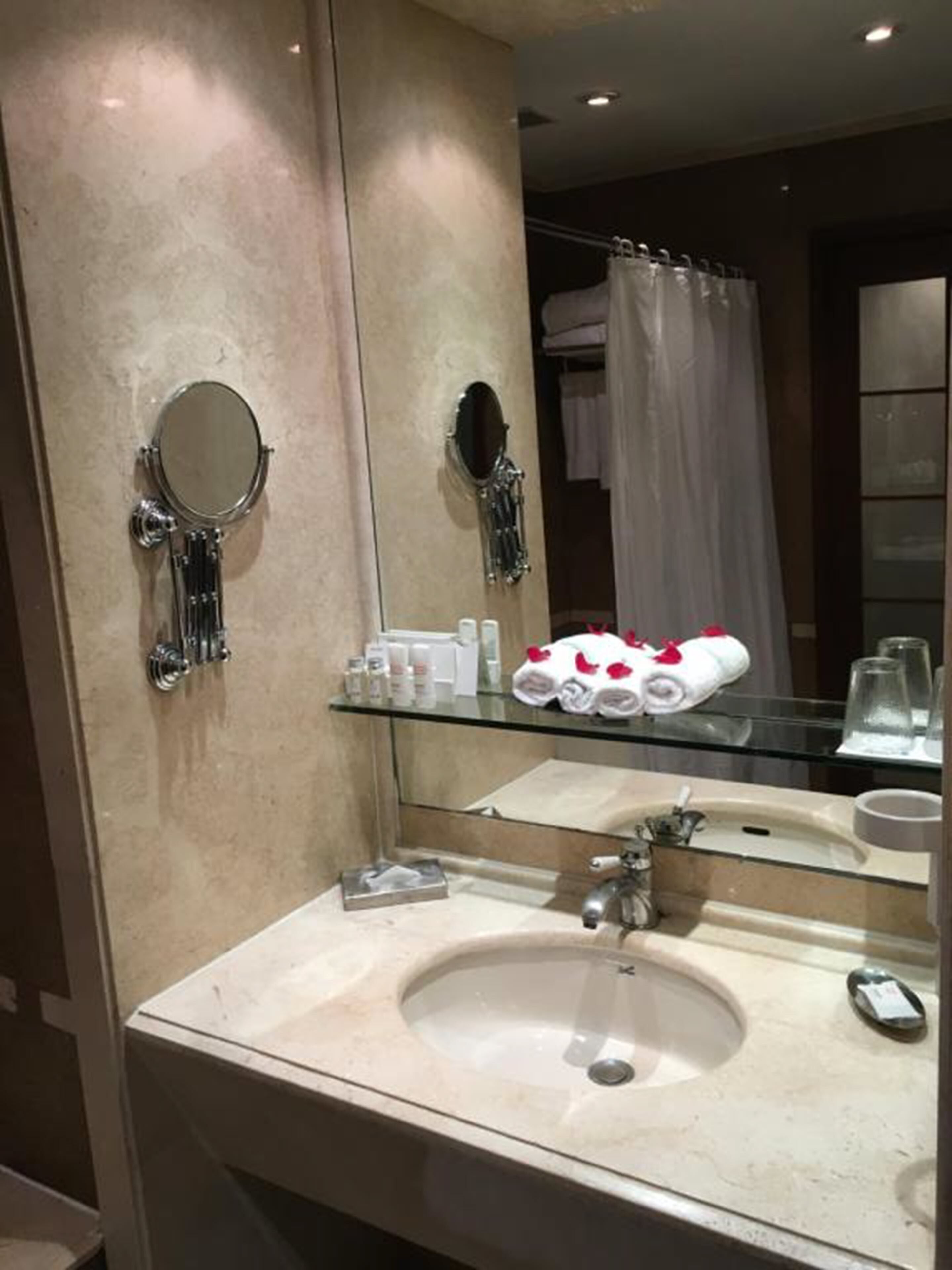 A modern bathroom with a large mirror, a glass shelf with toiletries, and a sink.