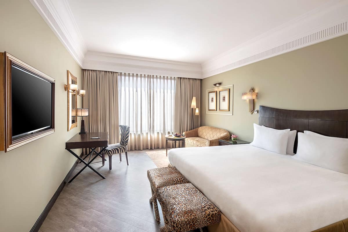 A hotel room with a large bed, a desk, a chair, a small table, and a TV.