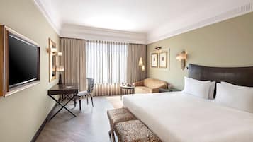 A hotel room with a large bed, a desk, a chair, a small table, and a TV.