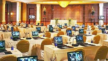 Un salón de conferencias con varias mesas dispuestas en filas, cada una equipada con computadoras portátiles y pantallas.