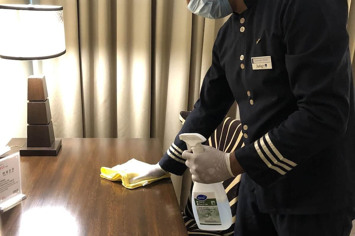 A hotel staff member cleaning a wooden table with a yellow cloth and a spray bottle.