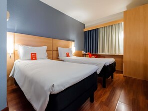 A hotel room with two beds, wooden headboards, a desk, and a window with curtains. - ibis Joinville (Joinville)