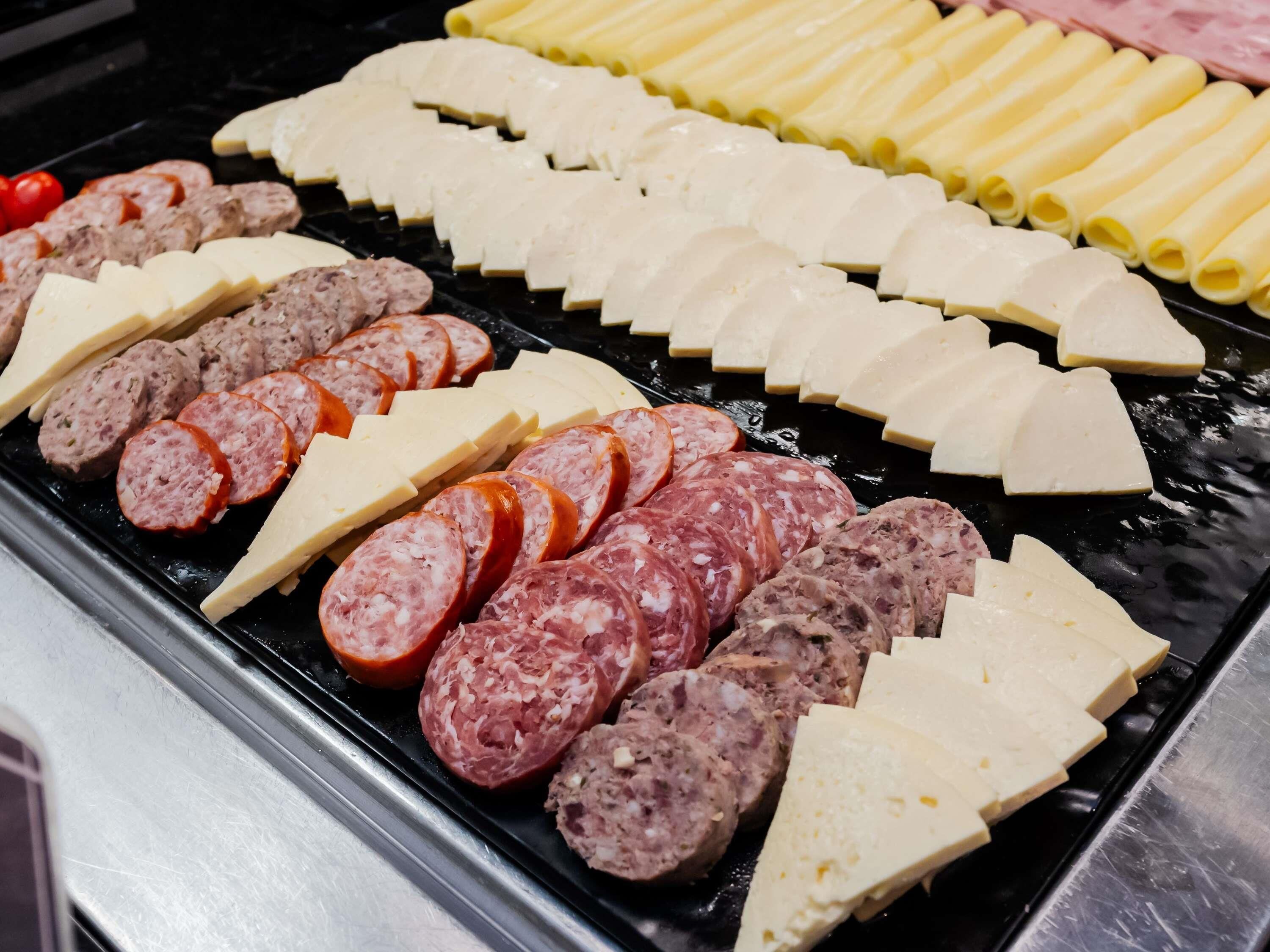 A variety of sliced meats and cheeses on a grill.