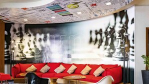 A modern lounge area with a red sofa, black and white chairs, and a chess table. - ibis Joinville (Joinville)